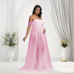 A pregnant woman wears a pink off-shoulder maternity maxi gown with a sheer mesh skirt.