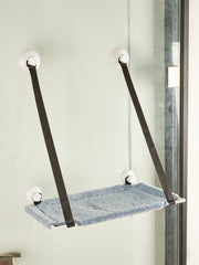 A blue fabric cat hammock suspended by four suction cups on a glass window.