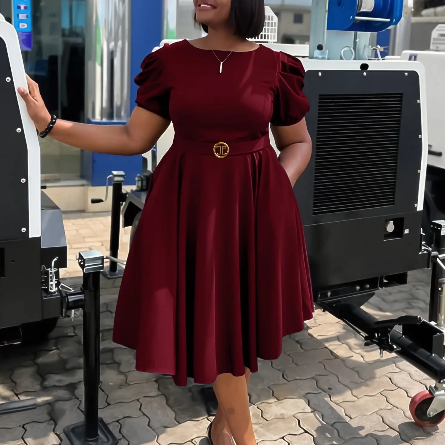 A woman wears a short-sleeved, burgundy pleated dress with a gold-buckled belt.