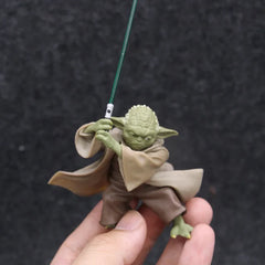 A small Yoda action figure from Star Wars holding a green lightsaber, held in a person's hand.