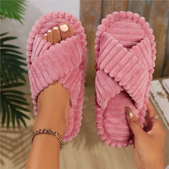 A pair of pink corduroy crossband slippers for women with a soft, fuzzy texture.