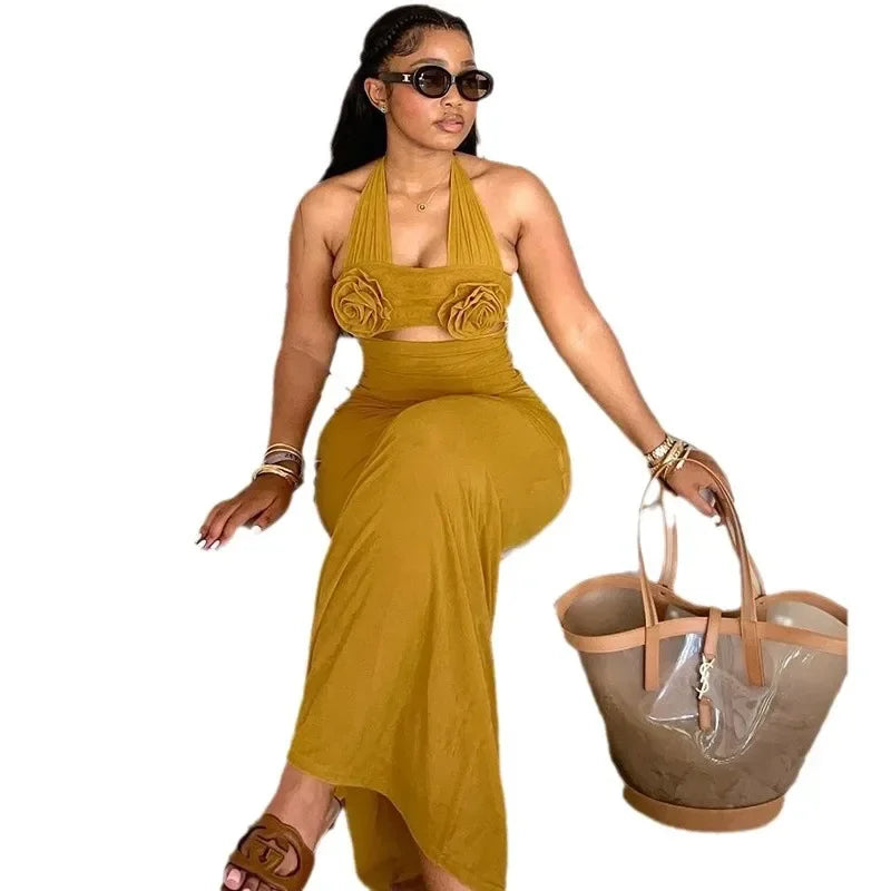 A woman wears a mustard yellow ankle-length halter dress featuring floral accents on the bodice.
