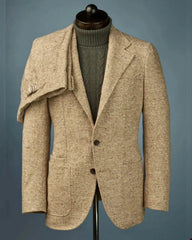 A tan wool tweed blazer with patch pockets worn over a dark green cable knit turtleneck sweater.