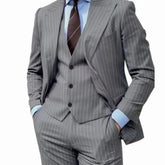 A man wears a grey pinstripe three-piece suit with a peak lapel blazer, vest, and trousers.