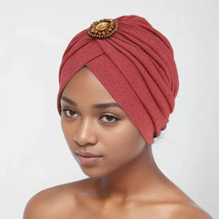 A woman wears a pleated, rust-colored turban cap adorned with a central decorative jewel.