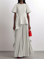 A model wears a floor-length white peplum dress with short sleeves and an irregular pleated hem.