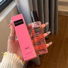 A hand holds a 100ml bottle of Peach Jo+ perfume with a textured, faceted glass design next to its matching pink box.