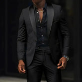 A man wears a black slim-fit two-piece suit featuring a shawl lapel blazer and matching trousers.