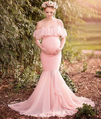 A pregnant woman wears a pink off-shoulder mermaid maternity gown with ruffle details.