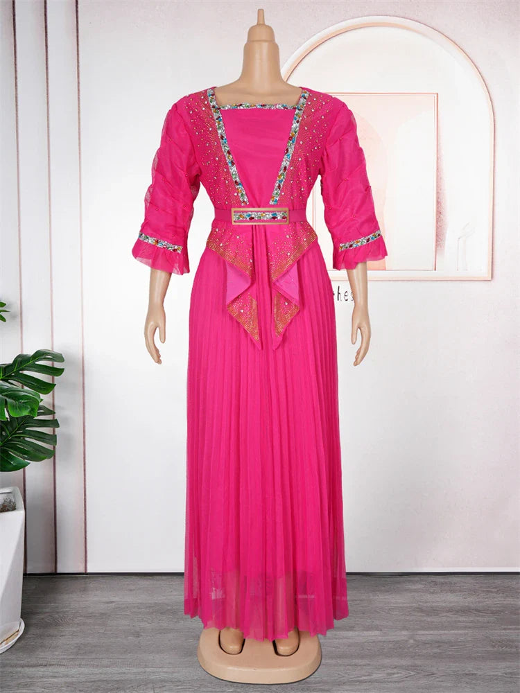 A bright pink pleated maxi dress with embellished trim and a matching belt on a mannequin.