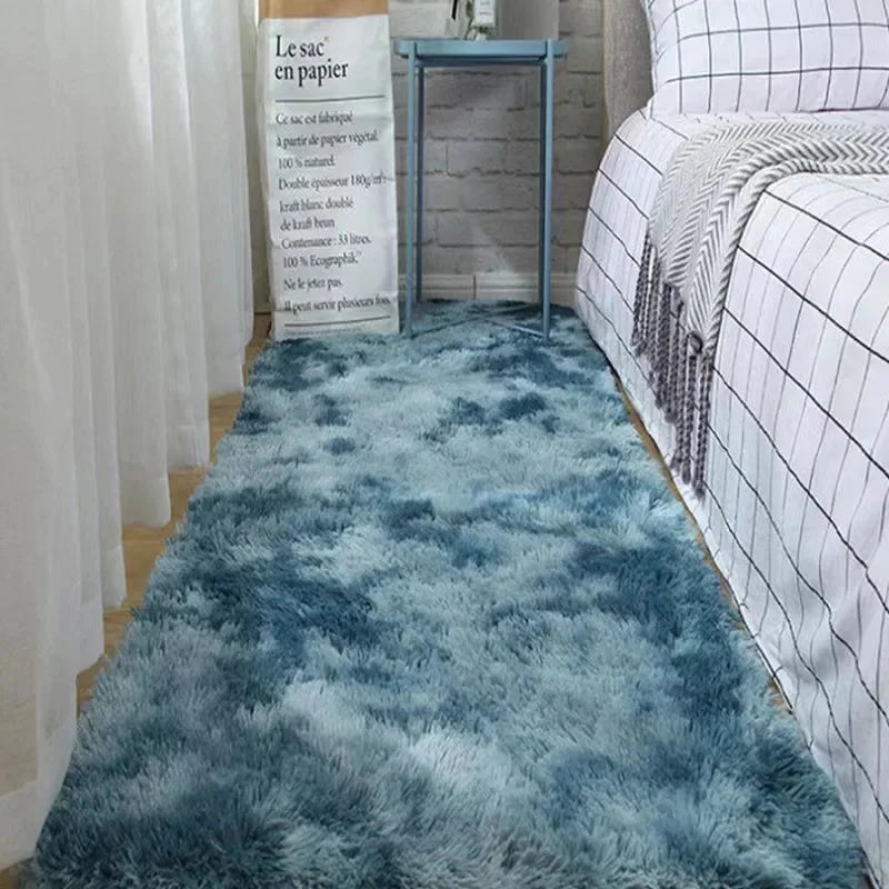 A rectangular, plush blue ombre rug lies on a bedroom floor beside a bed.