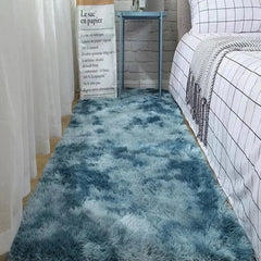 A rectangular, plush blue ombre rug lies on a bedroom floor beside a bed.