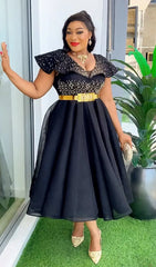A woman wears a black mid-calf A-line dress with rhinestone embellishments and a gold waist belt.