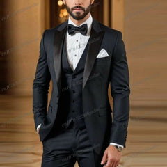 A man wearing a black three-piece tuxedo with a white shirt and a black bow tie.