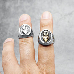 Two stainless steel rings featuring a Sacred Heart and cross design worn on a hand.