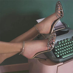 A pair of gold stiletto high heels with crystal-embellished straps and an ankle buckle closure.