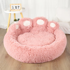 A round, pink, fluffy pet bed shaped like a paw with four white toe pads.