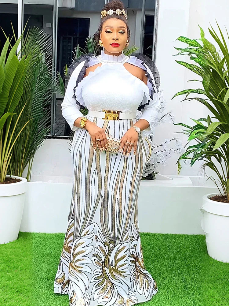 A woman wears a floor-length white and gold sequined African-style gown with puff sleeves.