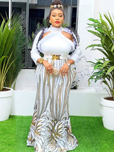 A woman wears a floor-length white and gold sequined African-style gown with puff sleeves.