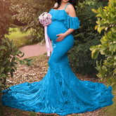 A pregnant woman wears a bright blue, floor-length lace maternity dress with an off-shoulder ruffle.