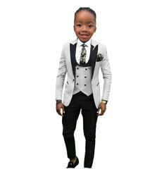 A young boy wears a three-piece formal suit featuring a white blazer, grey vest, and black pants.