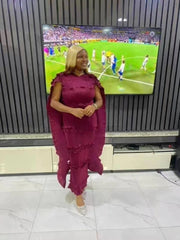 A woman wears a sleeveless, mid-calf length, pleated burgundy dress with tiered ruffle details.