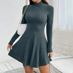 A woman wears a dark green, long-sleeved, mock neck mini dress with a flared A-line skirt.