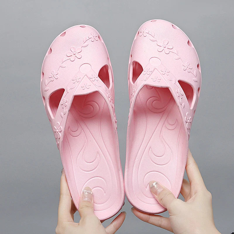A pair of light pink women's jelly slippers with floral cutouts and a flat sole.