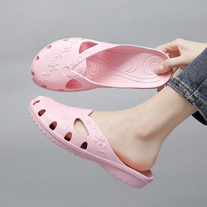 A pair of light pink, floral-patterned jelly slippers with cutouts being held by a person.