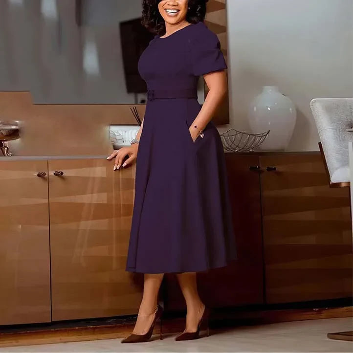 A woman wears a solid dark purple midi dress with short sleeves, a belted waist, and side pockets.