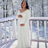 A pregnant woman wears a white long-sleeve lace V-neck maternity maxi dress outdoors in the snow.