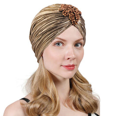 A woman wears a metallic gold pleated turban featuring a decorative cluster of brown beads.
