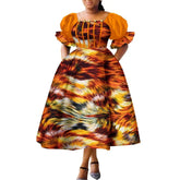 A woman wears an orange puff-sleeve midi dress with a vibrant, multi-colored abstract print.