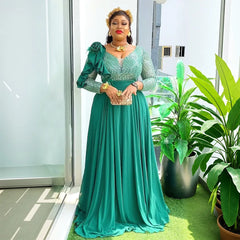 A woman wears a long-sleeved emerald green A-line maxi dress with a V-neck and ruffled shoulder.