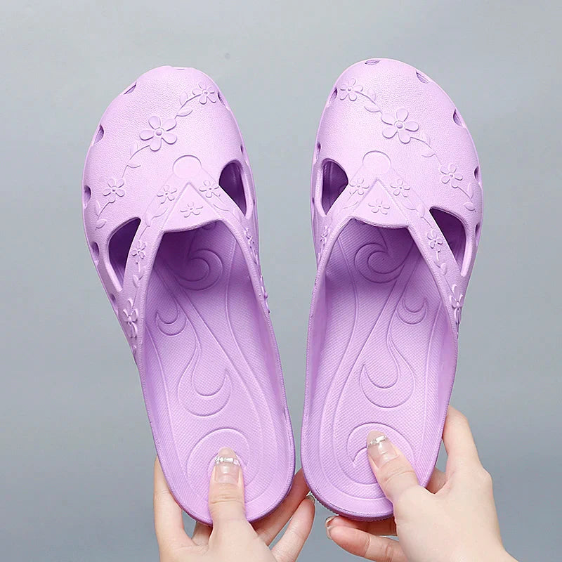 A pair of light purple women's jelly slippers with floral cutouts and a flat sole.