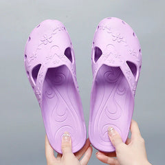 A pair of light purple women's jelly slippers with floral cutouts and a flat sole.