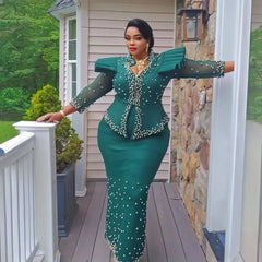 A woman wears an elegant emerald green two-piece suit featuring structured shoulders and pearls.