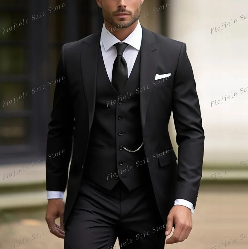 A man wearing a black three-piece suit with a matching vest, tie, and white pocket square.