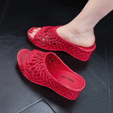 A pair of red wedge slippers with a hollow-out woven design and a thick platform sole.