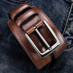 A brown textured leather belt for men with a silver rectangular buckle resting on dark denim.