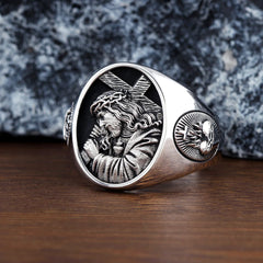 A silver ring featuring an embossed image of Jesus carrying the cross on a dark background.