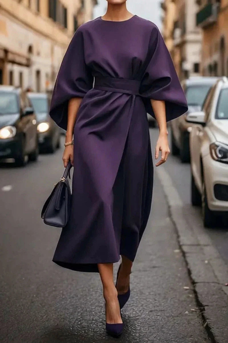 A woman wears an elegant ankle-length purple dress with bat sleeves and a cinched waist.
