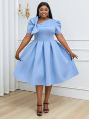 A woman wears a light blue, short-sleeved, pleated A-line dress with an asymmetrical bow neckline.