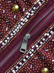 A close-up of a maroon garment featuring a silver zipper, white pearls, and gold embellishments.