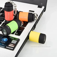 Four colorful, USB-rechargeable mini keychain flashlights are displayed on a laptop keyboard.