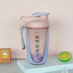 A light blue and pink protein shaker bottle with a carrying strap and internal mixing ball.