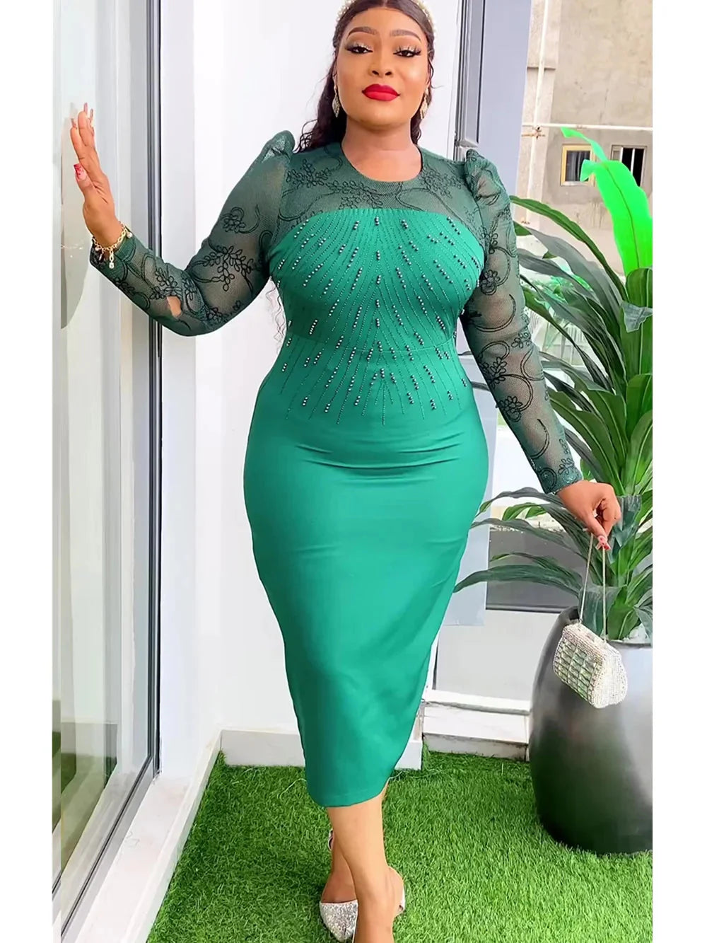 A woman wears a green midi dress with sheer lace sleeves and beaded embellishments on the bodice.