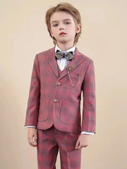 A boy wears a red plaid three-piece suit with a white shirt, a sparkly bow tie, and a lapel pin.