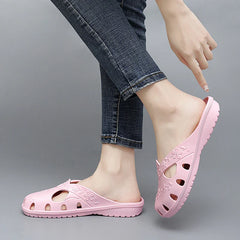 A pair of light pink, flat, breathable jelly slippers with floral cutouts worn by a person.