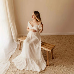 A pregnant woman wears a white off-shoulder bohemian maxi dress with ruffled details.